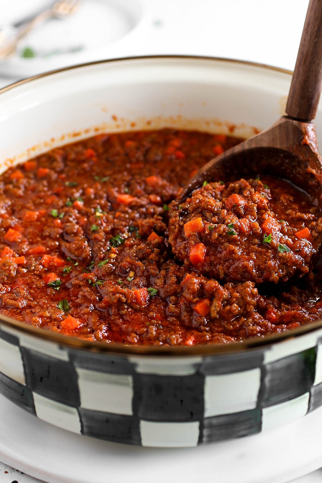 A spoon lifting a rich mince sauce from a cooking pot